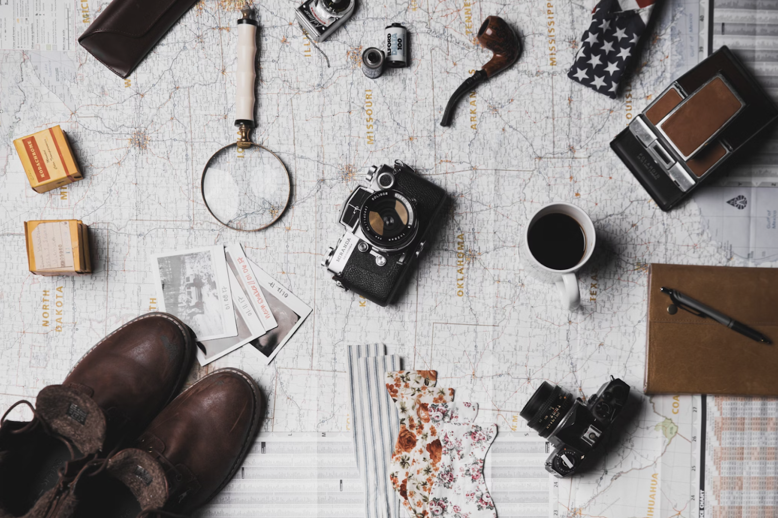 camera-hiking-boots-pipe-mug-magnifying-glass-and-tickets-on-map